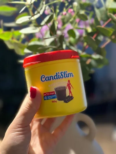 Mano que sostiene el bote amarillo de CandiSlim delante de una planta
