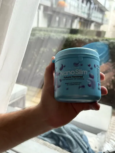 Mano que sujeta el bote azul de Nano Slim junto a una ventana