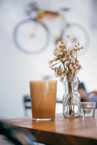 Vaso de batido sobre una mesa de madera, junto a un jarrón de flores secas