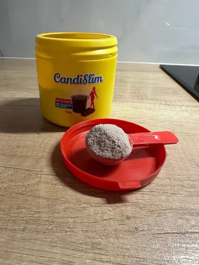 Bote de CandiSlim junto a su tapa roja, con el cacito lleno de polvo