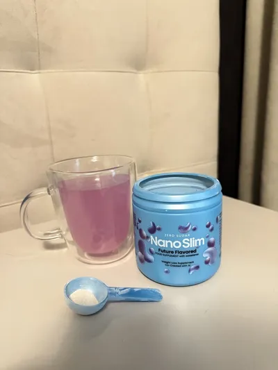 Taza de cristal con Nano Slim disuelto, de color rosa violáceo, junto al bote y el cacito
